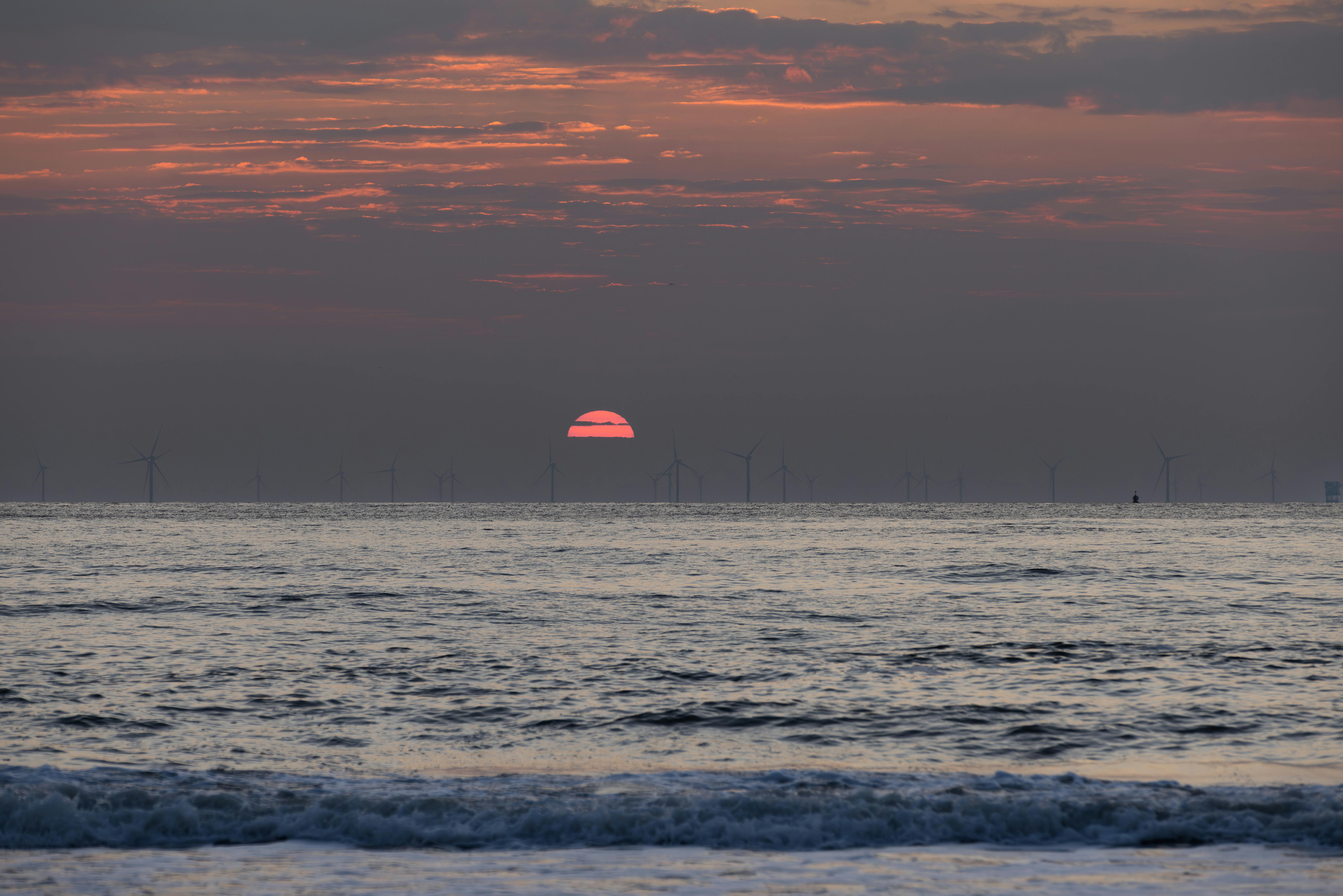 A stunning seaside sunset with silhouetted wind turbines on the horizon, capturing natural beauty and renewable energy.