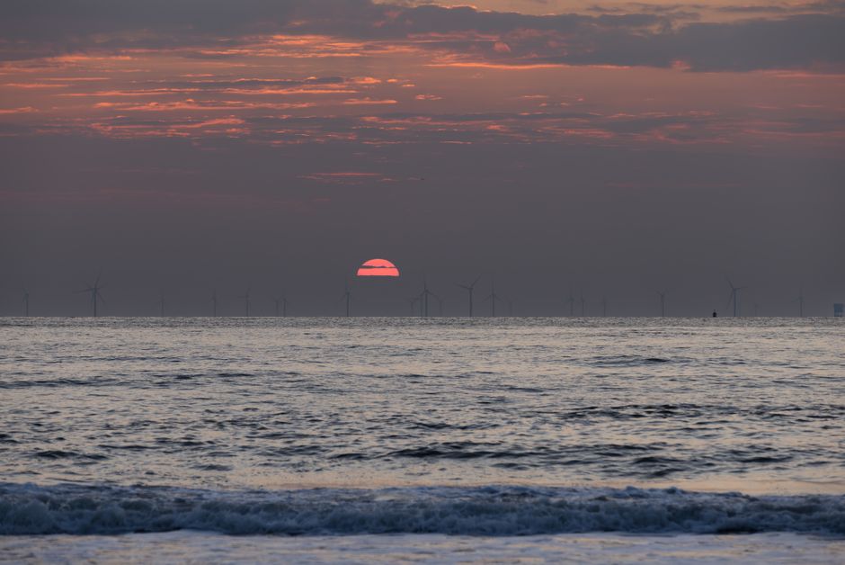 A stunning seaside sunset with silhouetted wind turbines on the horizon, capturing natural beauty and renewable energy.