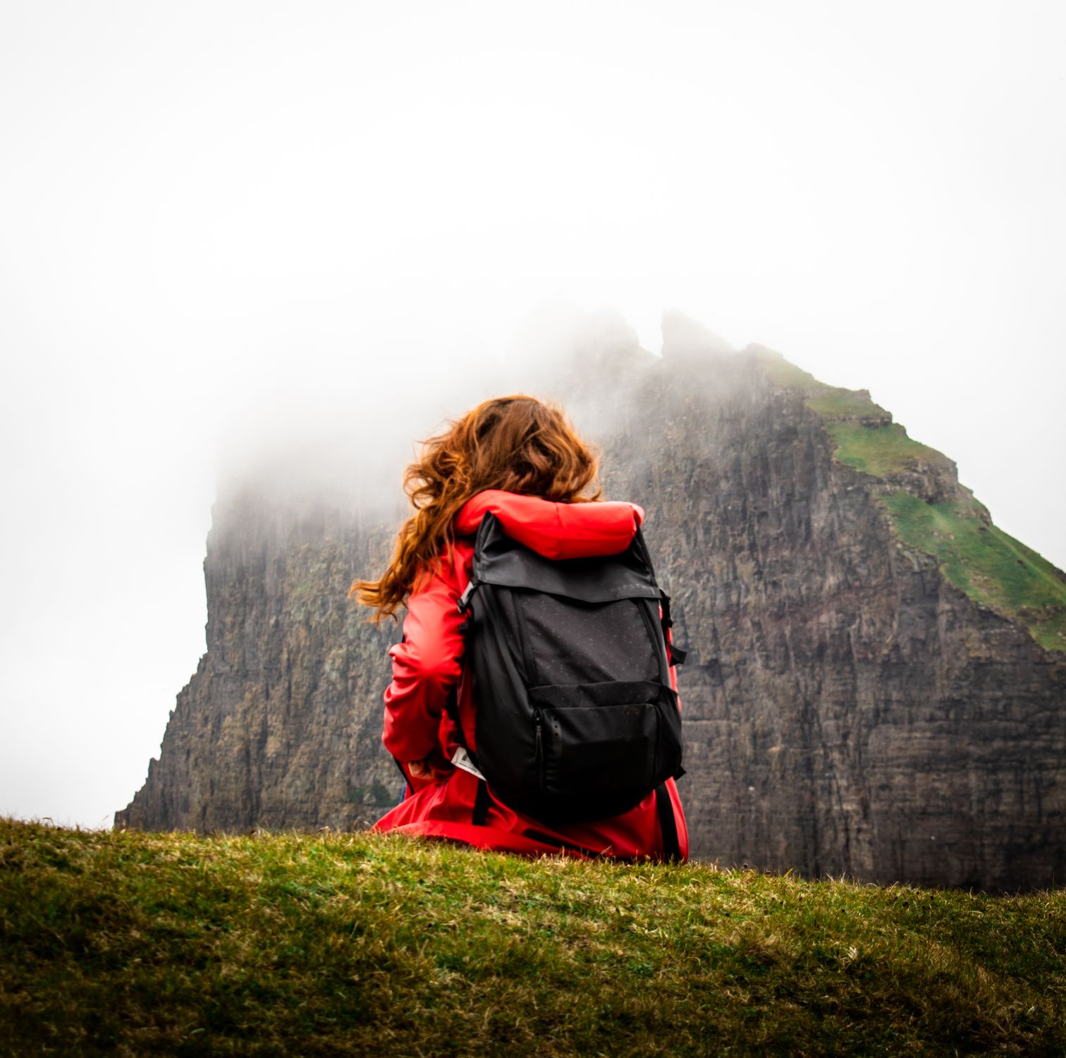 Back view of a woman carrying a backpack across a mountain covered by clouds in the Faroe Islands