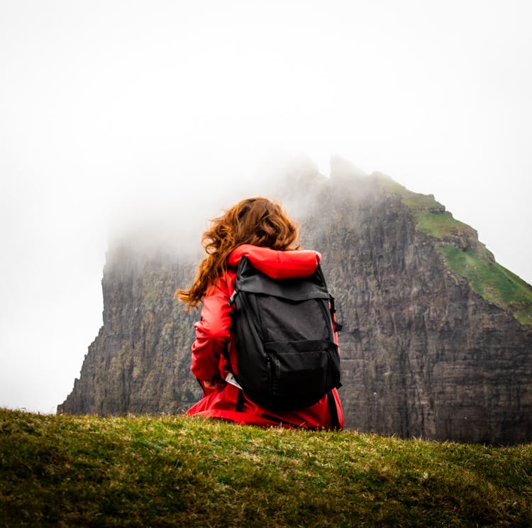 Back View Of A Woman Carrying A Backpack Across The Mountain Covered By Clouds