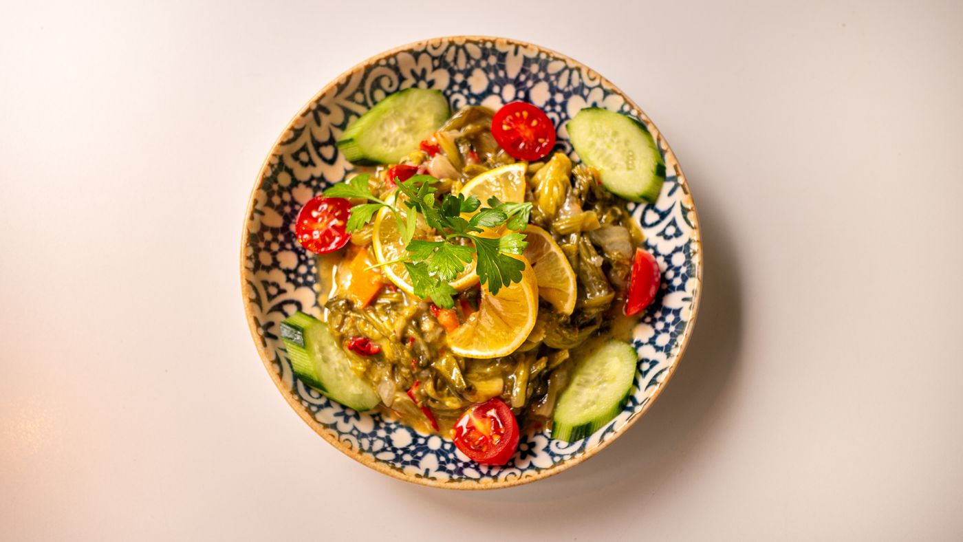 Top view of a vibrant vegetable salad with lemon, cucumber, and parsley in a decorative bowl.