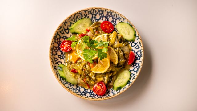 Top view of a vibrant vegetable salad with lemon, cucumber, and parsley in a decorative bowl.