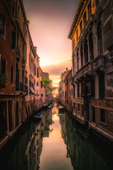 Captivating sunset view reflected on a serene Venetian canal amidst historic architecture. by Pixabay