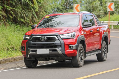 Free Close-up of a red pickup truck driving on a curved mountain road surrounded by lush greenery. Stock Photo