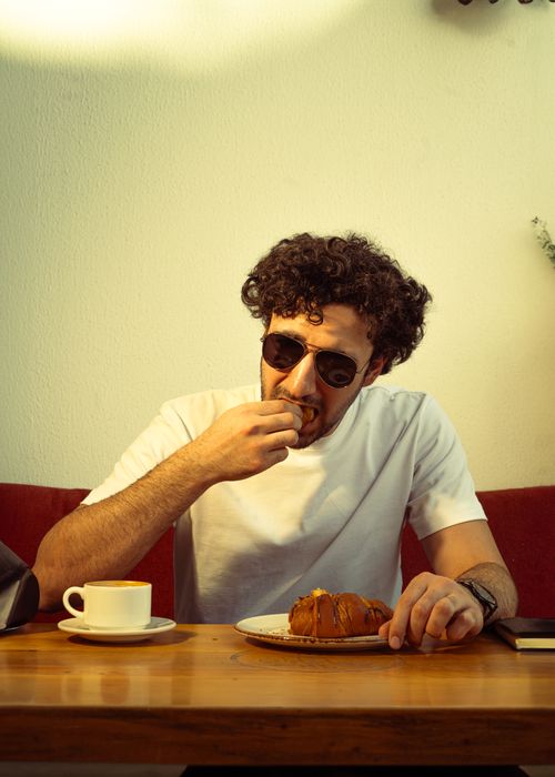 Free Man enjoying a croissant and coffee at a cozy indoor cafe, Baghdad Stock Photo