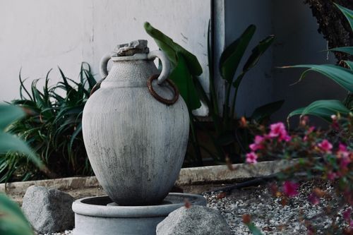 Free A large stone vase serves as a focal point in a serene garden, surrounded by greenery and flowers. Stock Photo