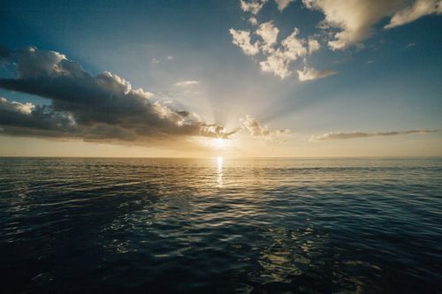 Free Peaceful ocean view at sunset with rays breaking through dramatic clouds. Stock Photo