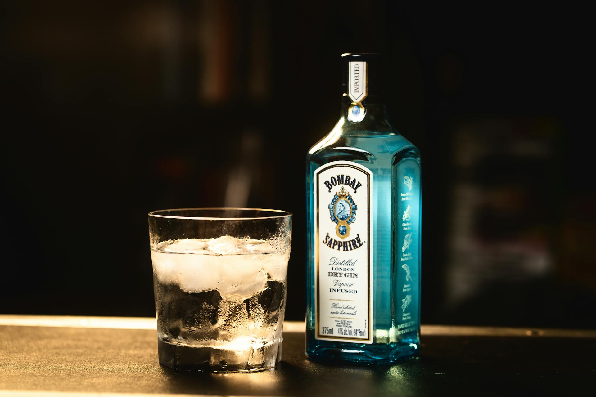 Chilled Bombay Sapphire gin bottle beside a glass of ice cubes, perfect for cocktails.