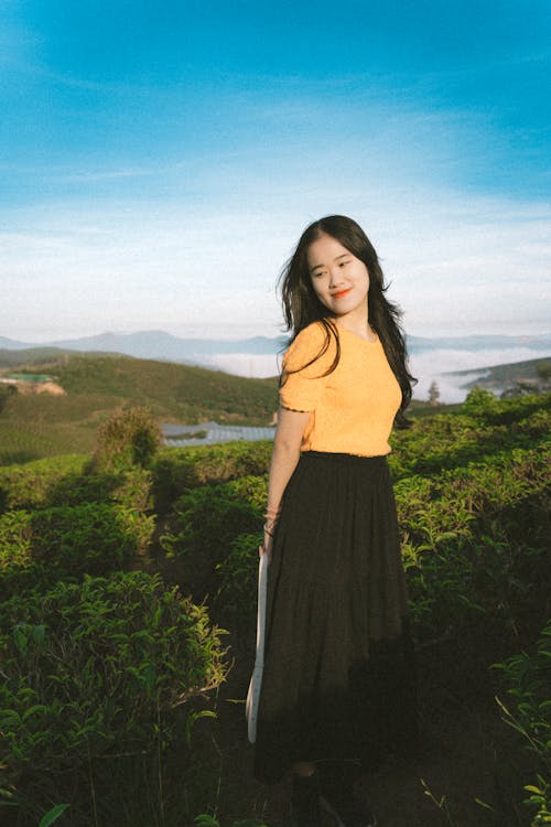 A woman in a yellow top and black skirt standing on a hill