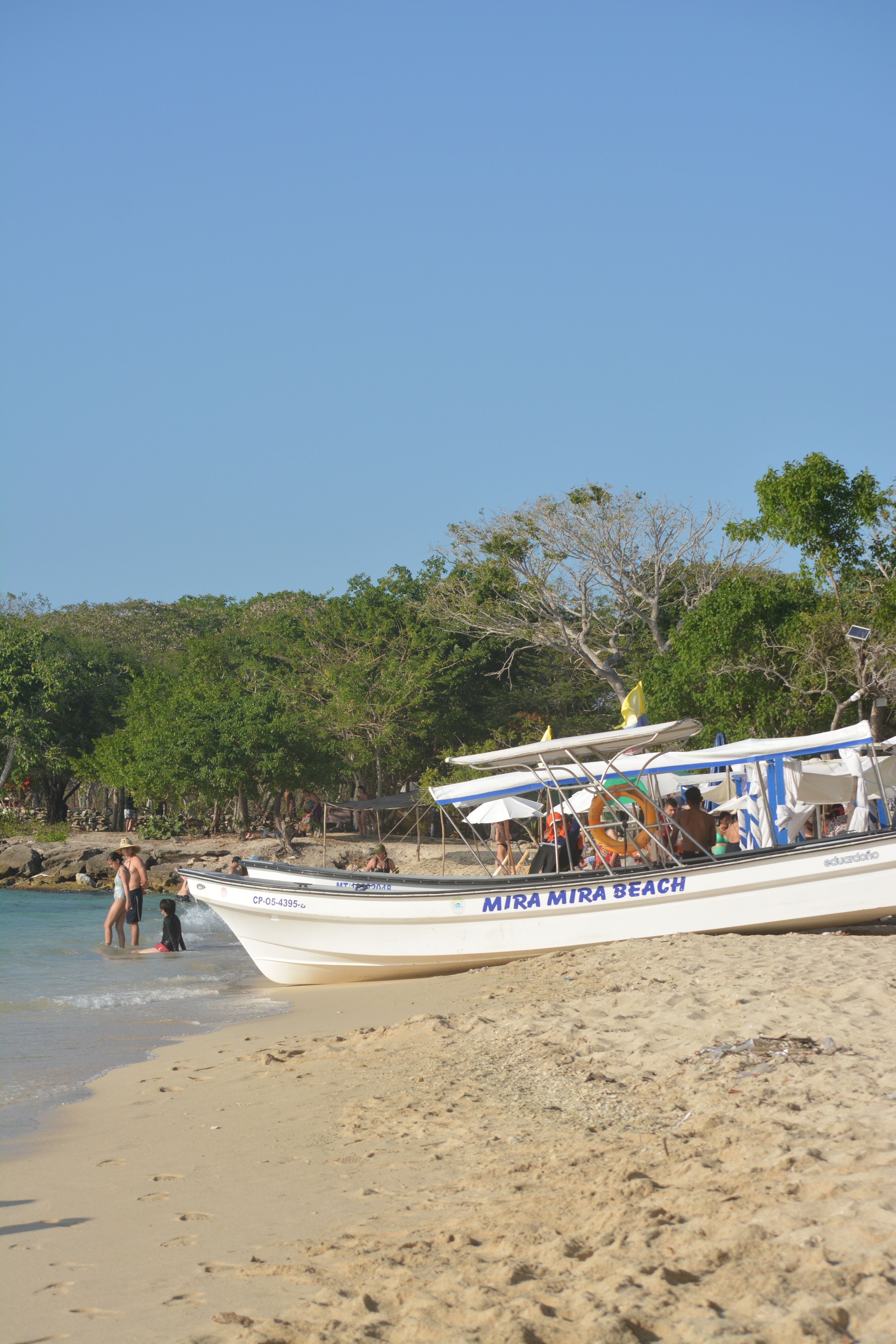 A sunny day at Mira Mira Beach featuring a boat and tourists enjoying the sandy shore.