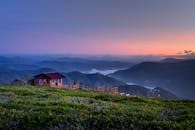 日出时分，薄雾笼罩着山丘和郁郁葱葱的绿色植物，宁静的山区景观中坐落着乡村木屋