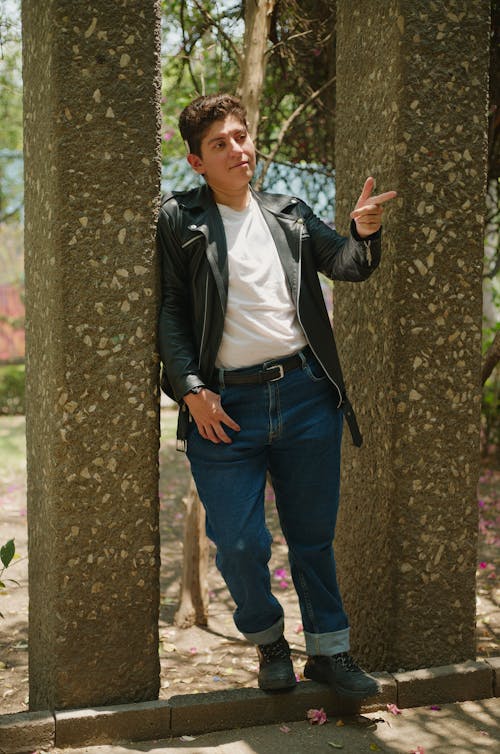 A man in jeans and a leather jacket leaning against a pillar