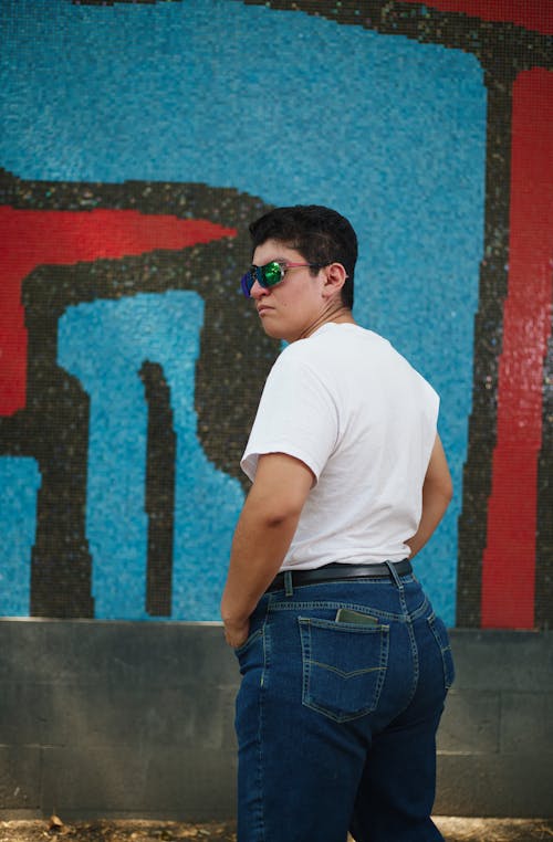 A man in jeans and a white shirt standing in front of a blue wall