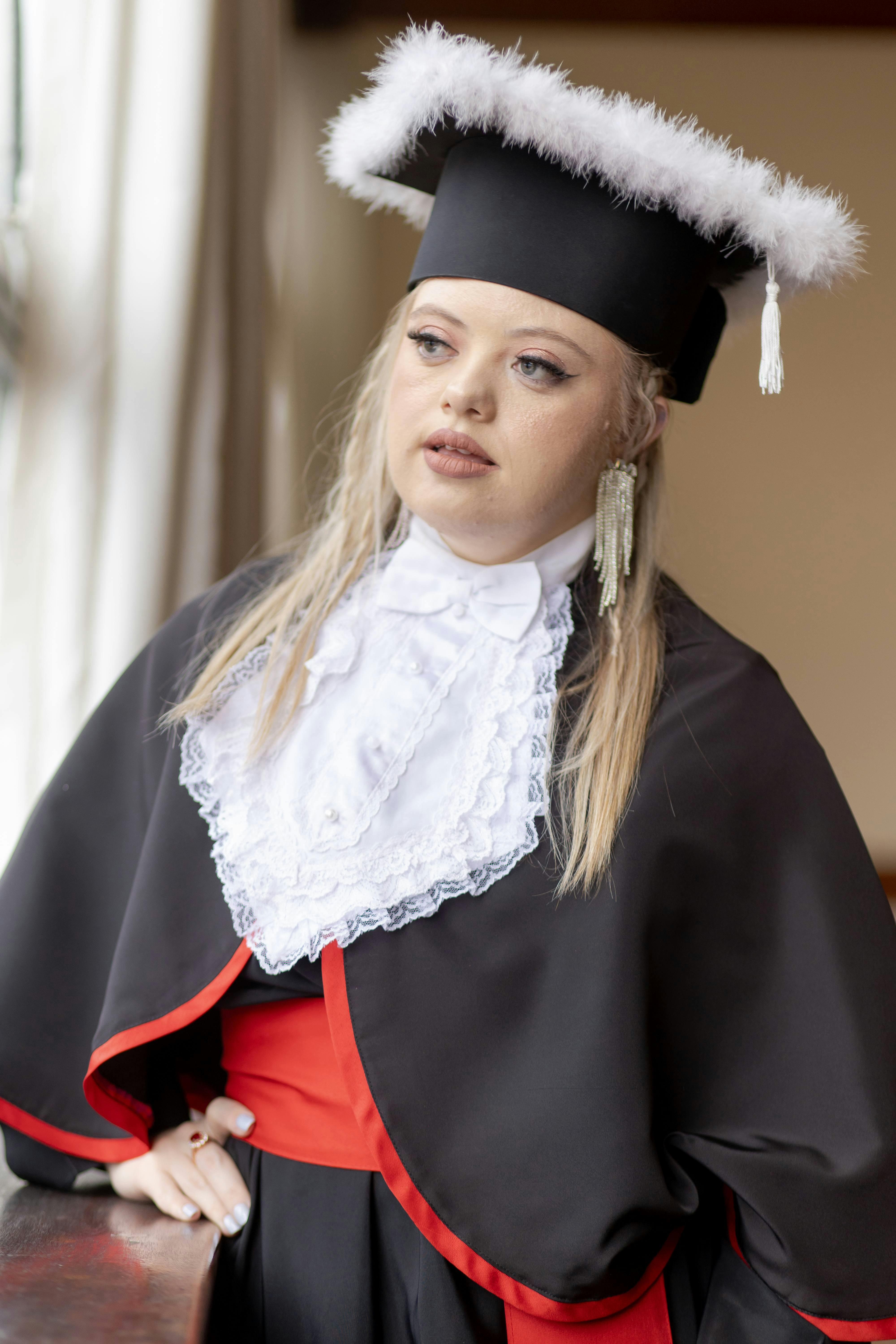 Young woman in traditional graduation attire gazing thoughtfully out the window.