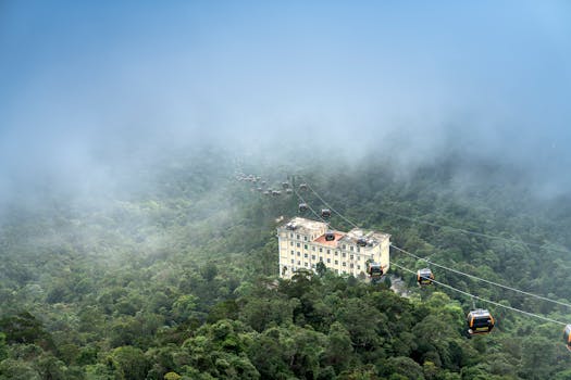 缆车行驶在云雾缭绕的山间森林上空，鸟瞰图中可见一栋建筑