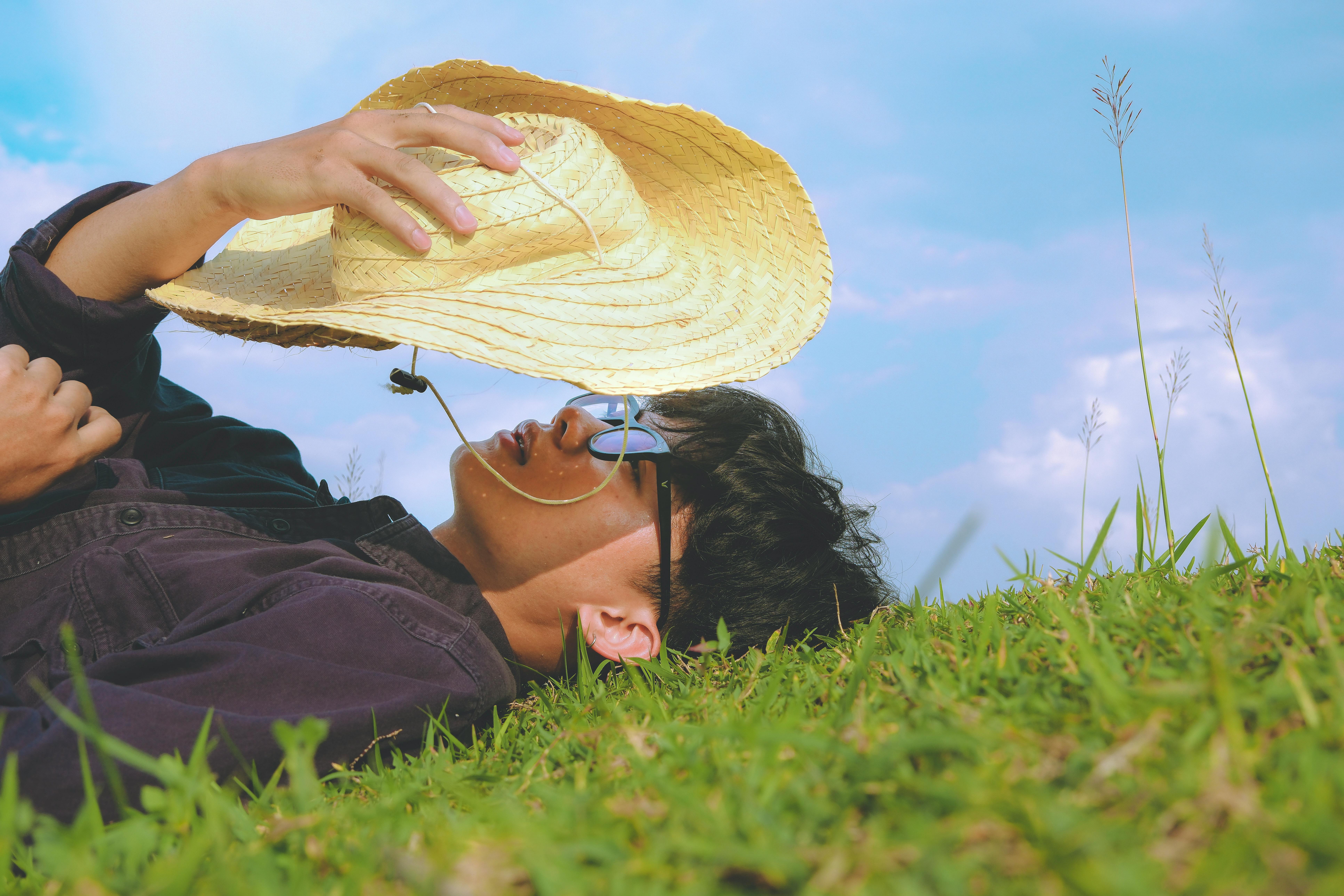 A man lying on grass with a straw hat and sunglasses, enjoying a sunny day.