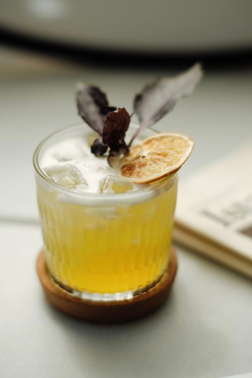 Free A refreshing yellow cocktail with ice, garnished with a dried lemon slice and herbs, on a coaster. Stock Photo