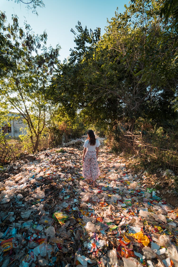 Photo Of A Woman Standing On A Pile Of Garbage Near Trees