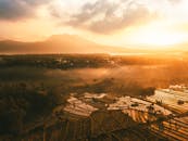 日出时分，从空中俯瞰巴厘岛，阳光下的水稻梯田与薄雾笼罩的山脉构成壮丽景色