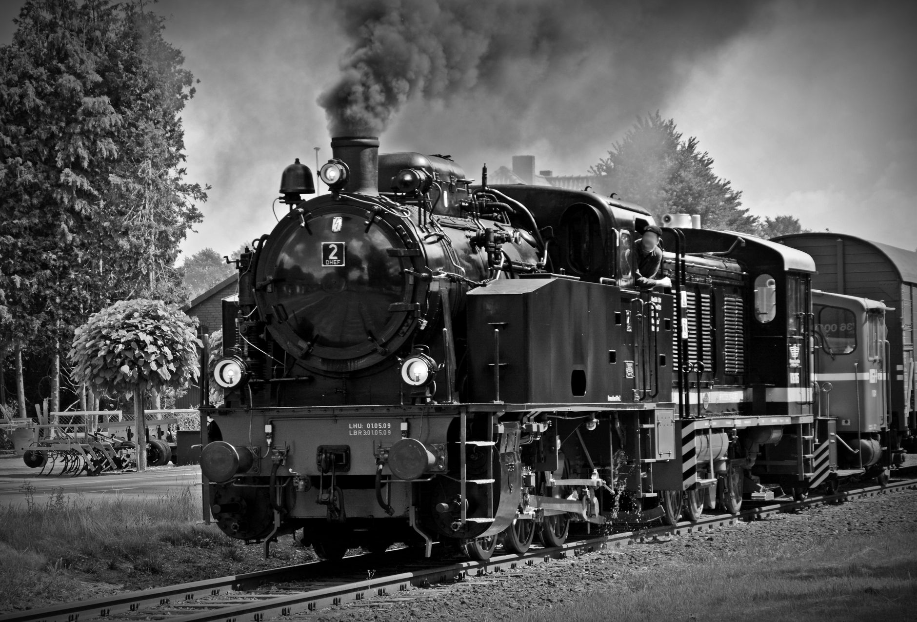 Black and white photo of a classic steam locomotive emitting smoke, evokes nostalgia for historical train travel. — free online jigsaw puzzle on JigsawPuzzlesFreeOnline.org