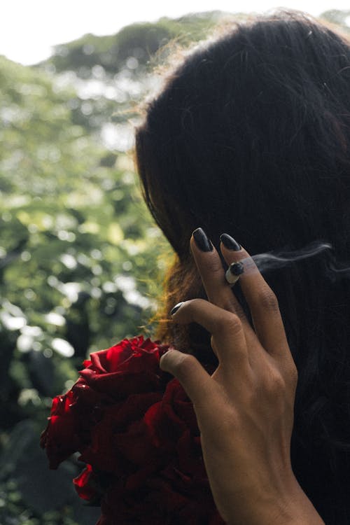 A woman smoking a cigarette with a rose in her hand