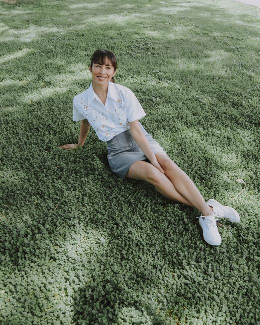 Smiling woman sitting on grass in a park, enjoying a sunny day.