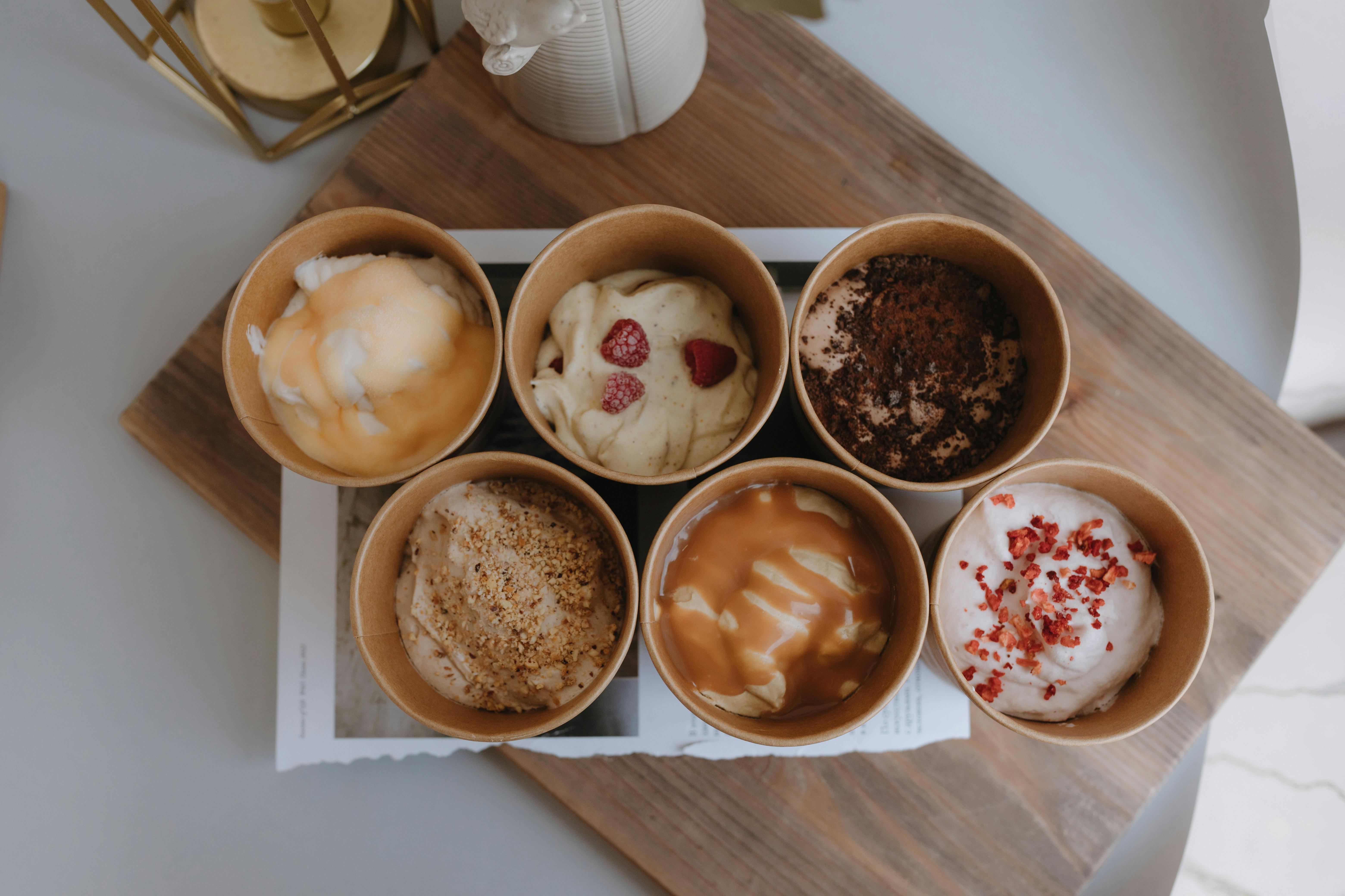 Top view of six assorted gourmet ice creams in paper cups on wooden tray.