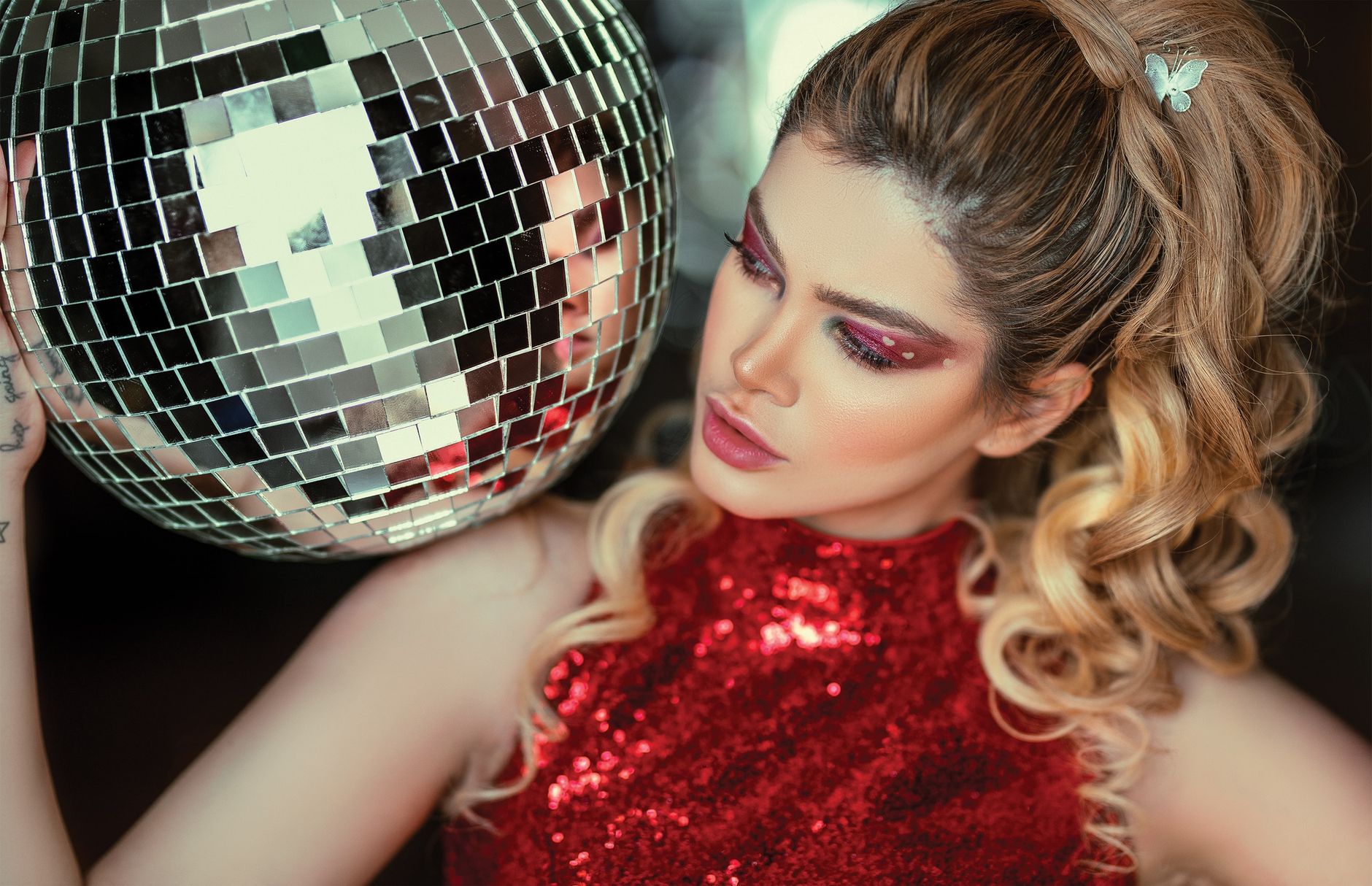 A glamorous woman in a red dress poses with a disco ball, showcasing fashion and beauty.
