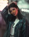 时尚的女人在夜间拍摄时，自信地戴着太阳镜、穿着牛仔夹克合影