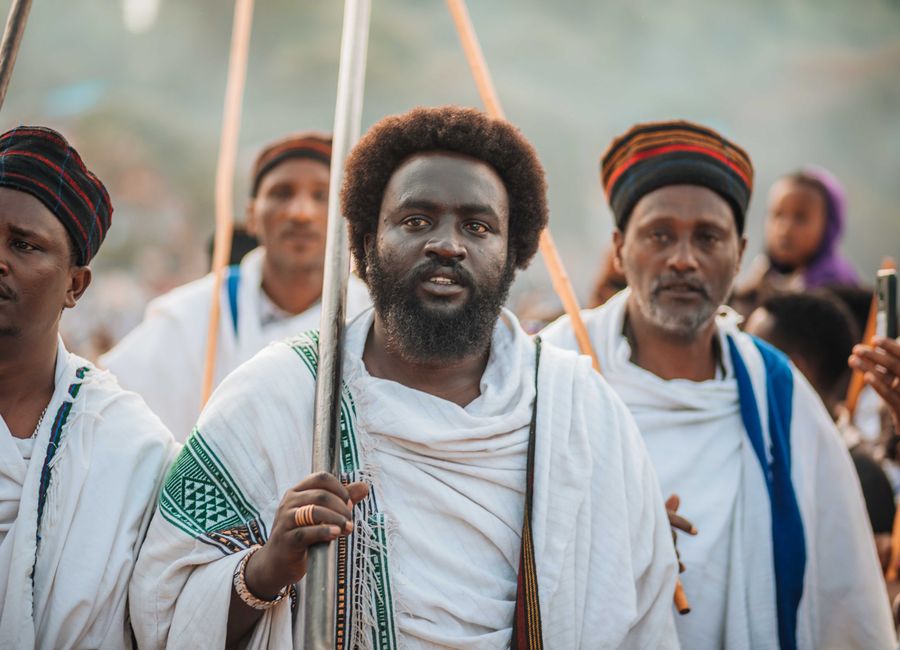 Men wearing traditional robes participate in a cultural event, holding wooden staffs.