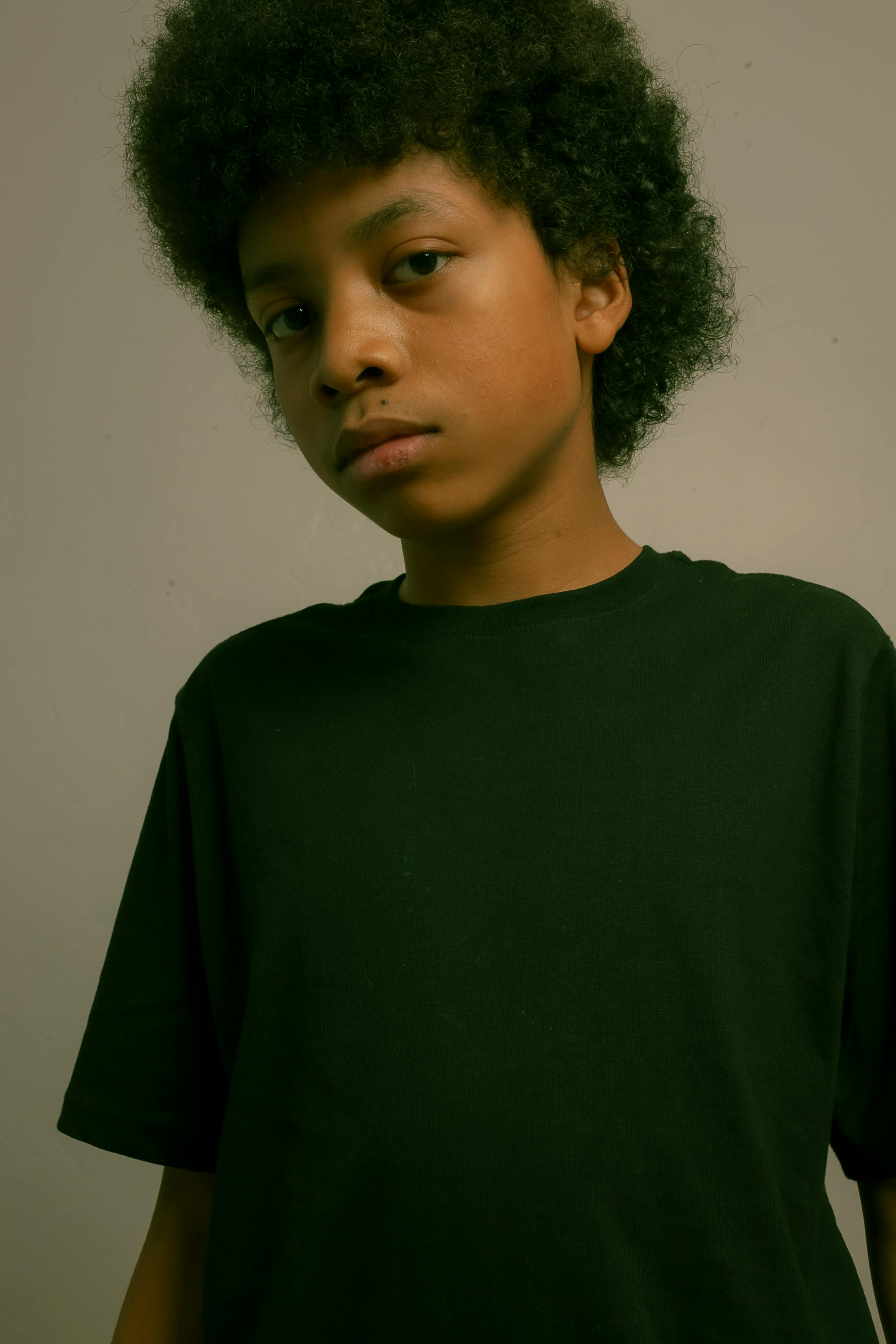 Young boy with curly hair in a black t-shirt posing indoors.