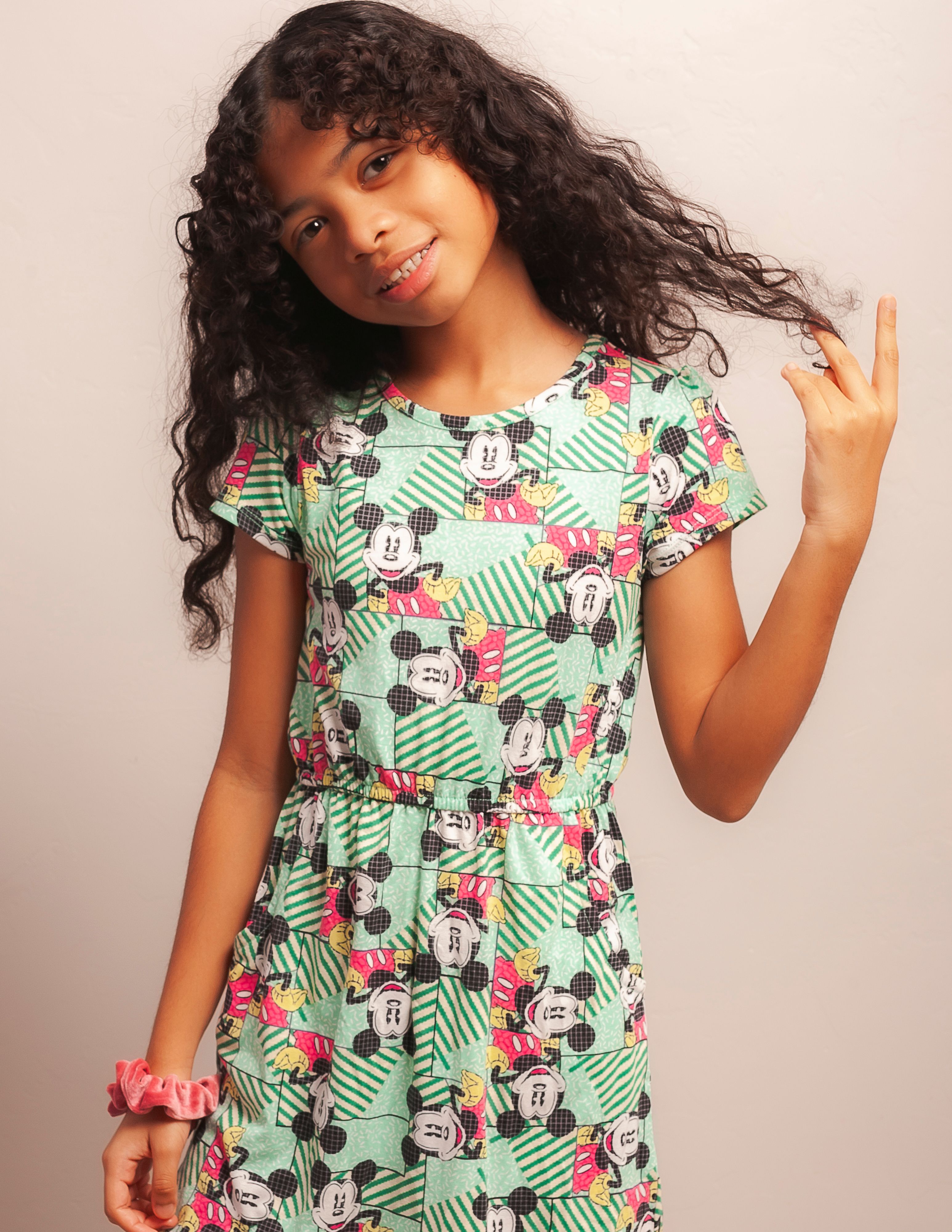 Portrait of a teenage girl with long curly hair in a colorful dress, smiling indoors.