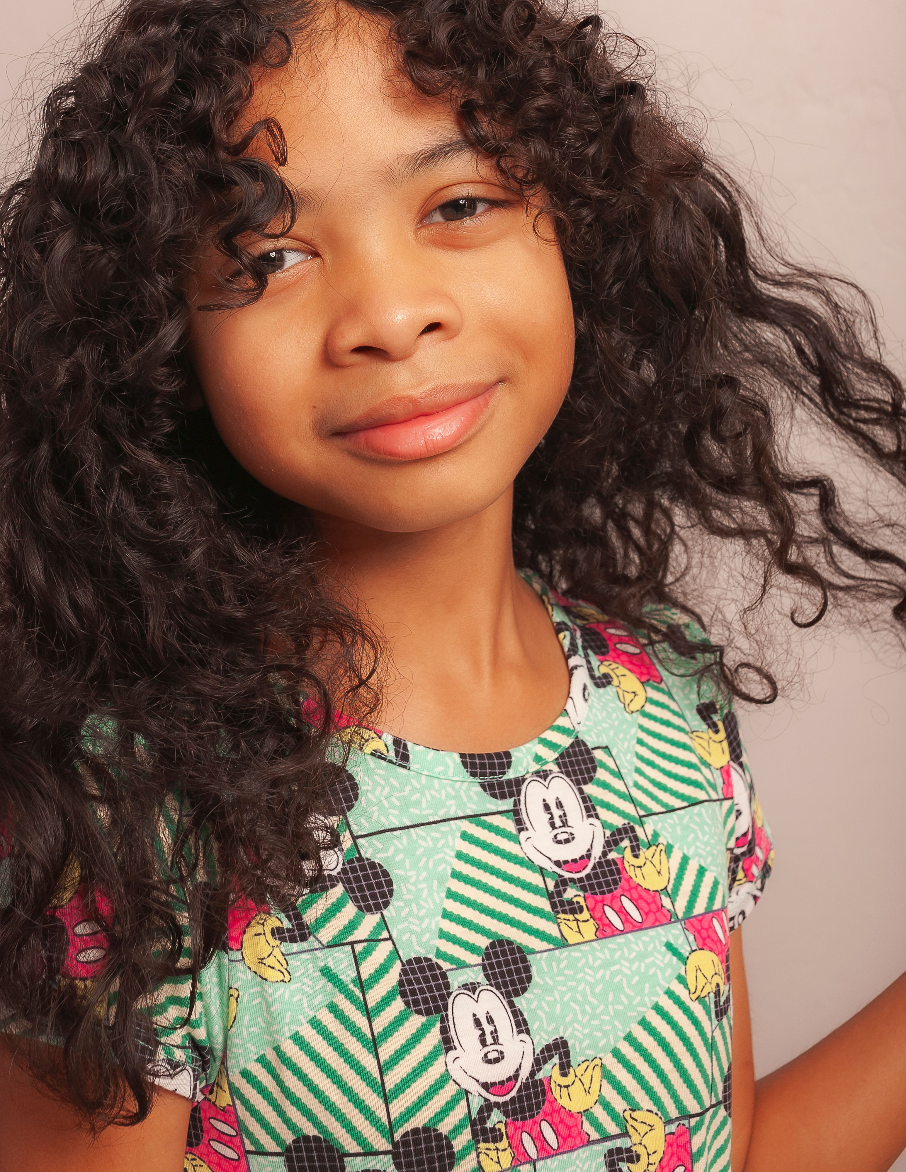 Studio portrait of a cheerful young girl with curly hair wearing a playful Disney-themed outfit.