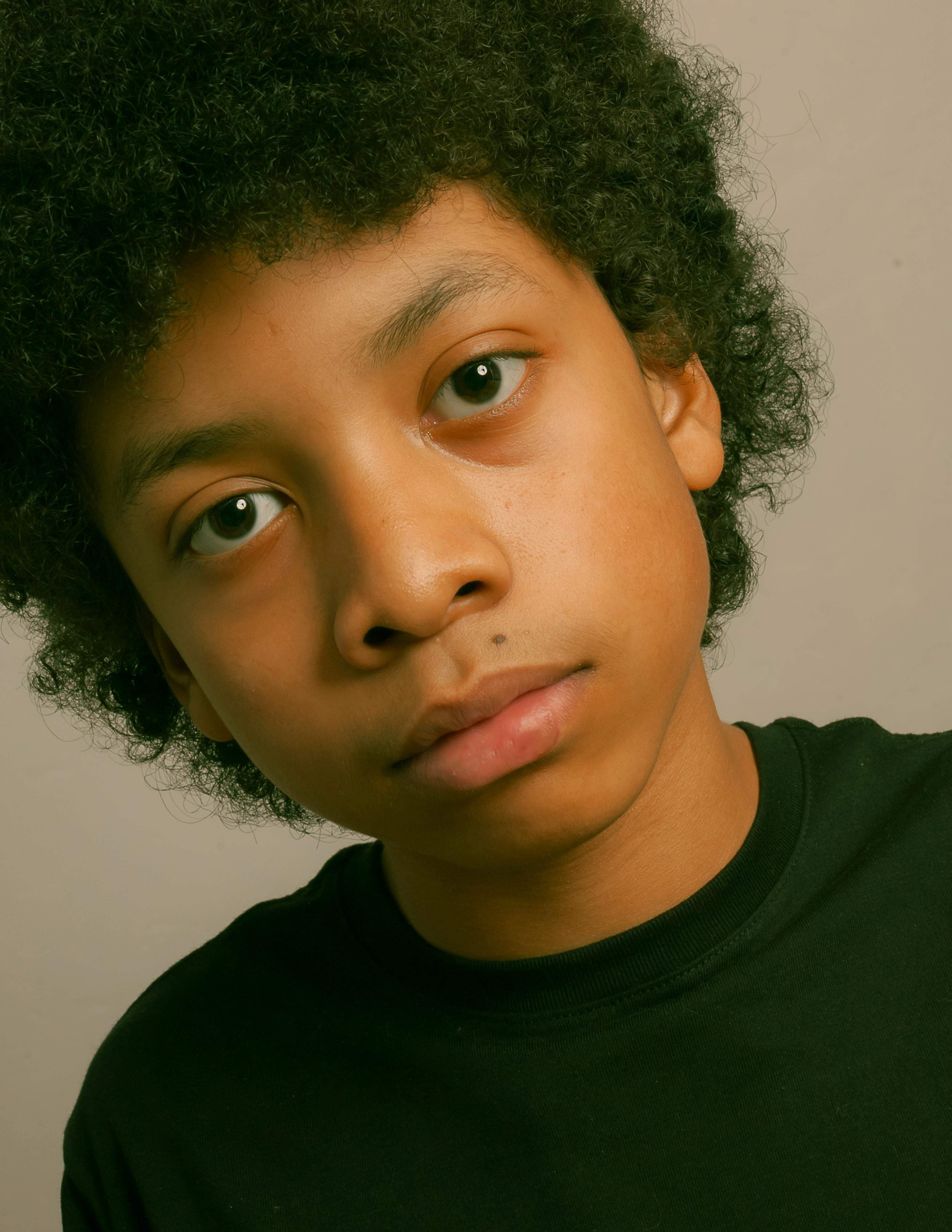Close-up portrait of a young curly-haired boy wearing a black t-shirt, captured indoors in Los Angeles.