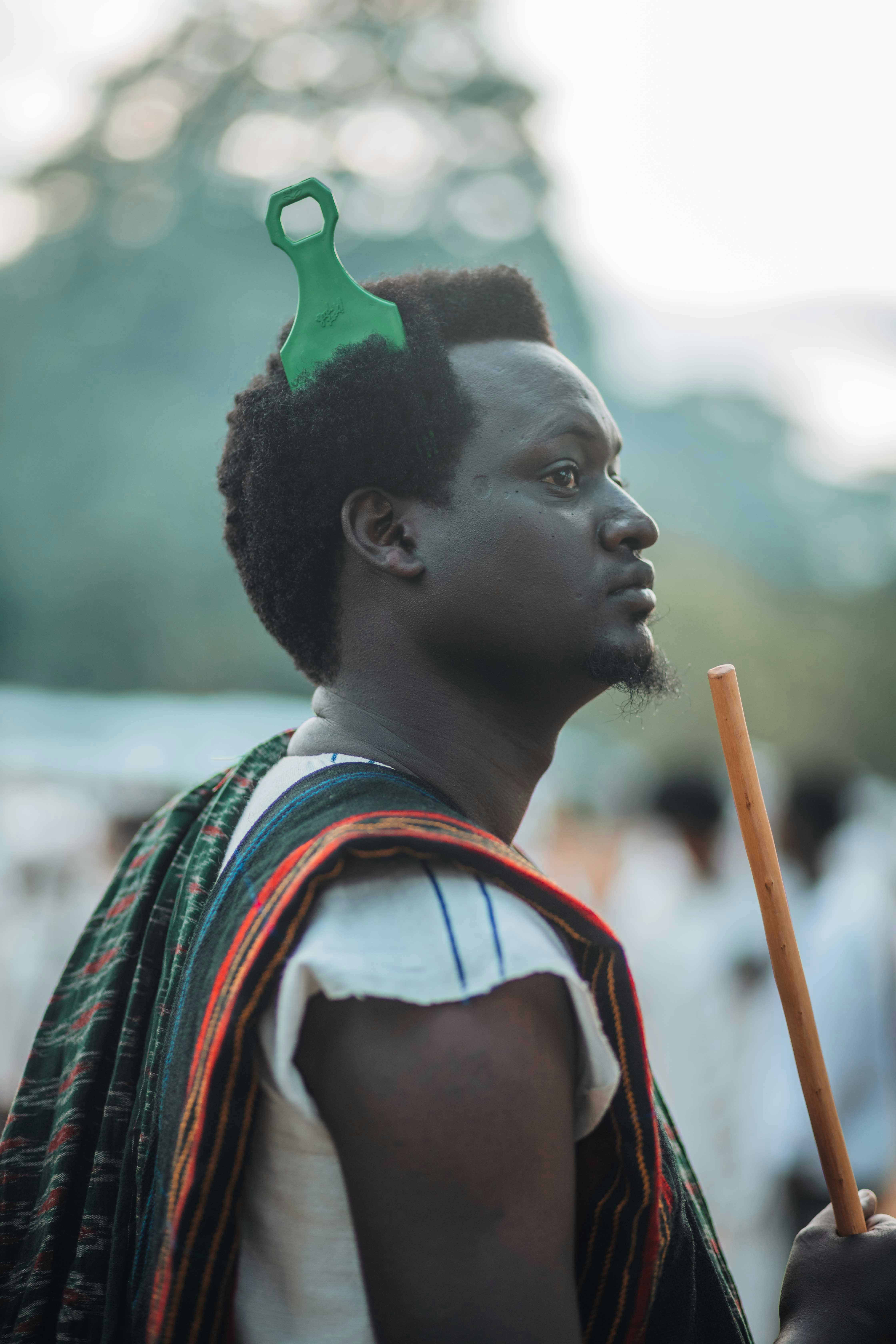 Profile portrait of a man with a stick and traditional attire outdoors.