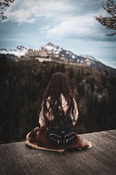 A woman sitting on a wooden deck gazing at the Austrian Alps, reflecting in solitude.