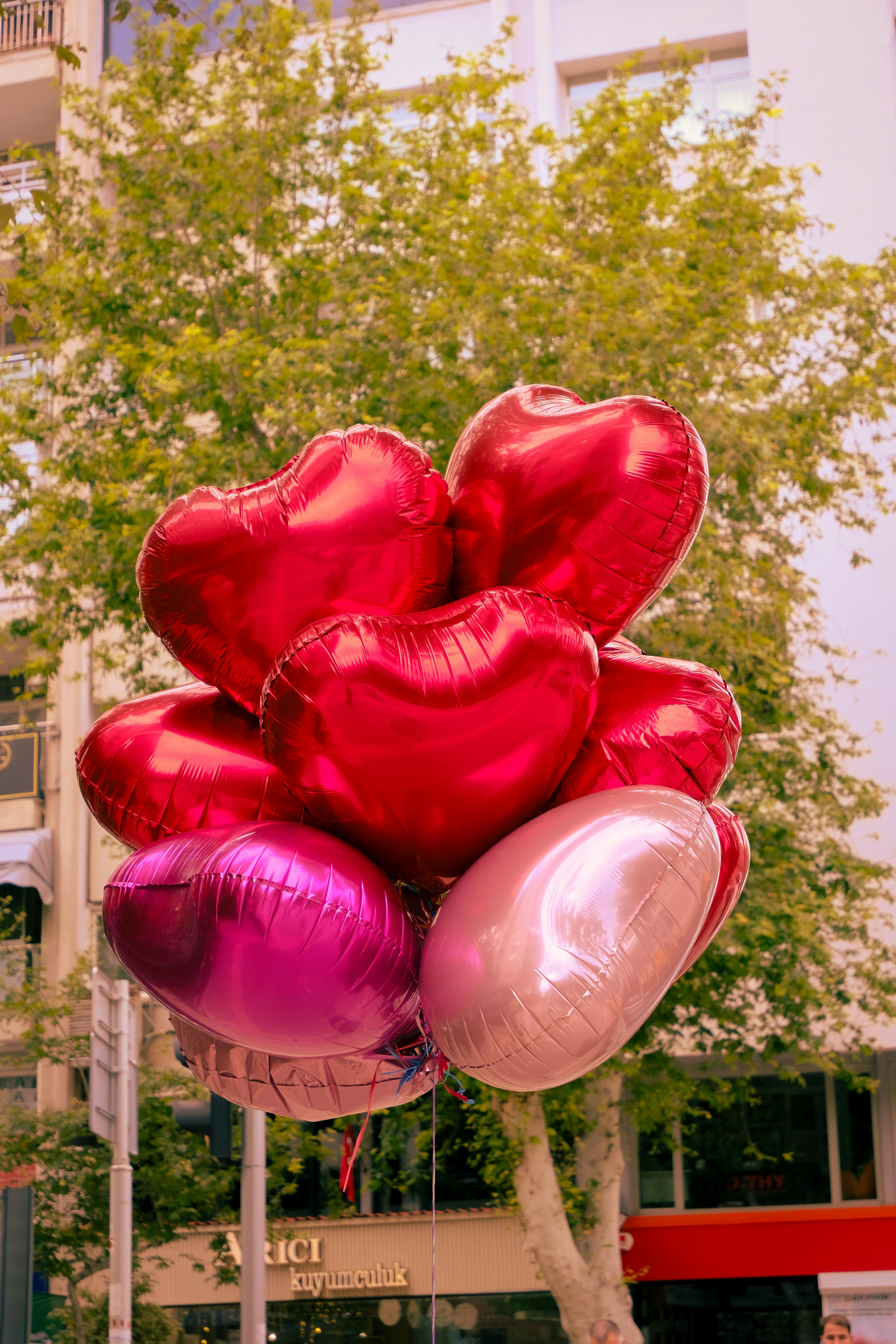 A colorful bunch of heart-shaped balloons floating outdoors in a vibrant urban setting.