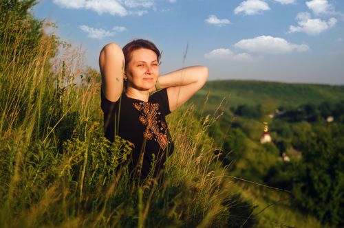 Free Woman in an embroidered blouse relaxing on a summer hillside, enjoying the scenic rural view. Stock Photo