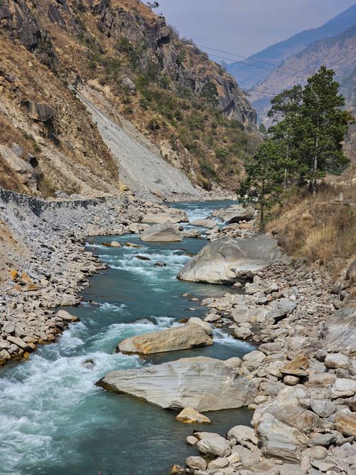 Free Tranquil river flows through a rocky mountain valley, surrounded by lush greenery and rugged terrain. Stock Photo