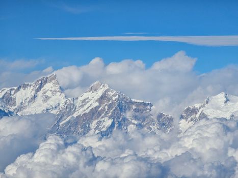 Majestic snowcapped mountains rising through the clouds under a vivid blue sky.