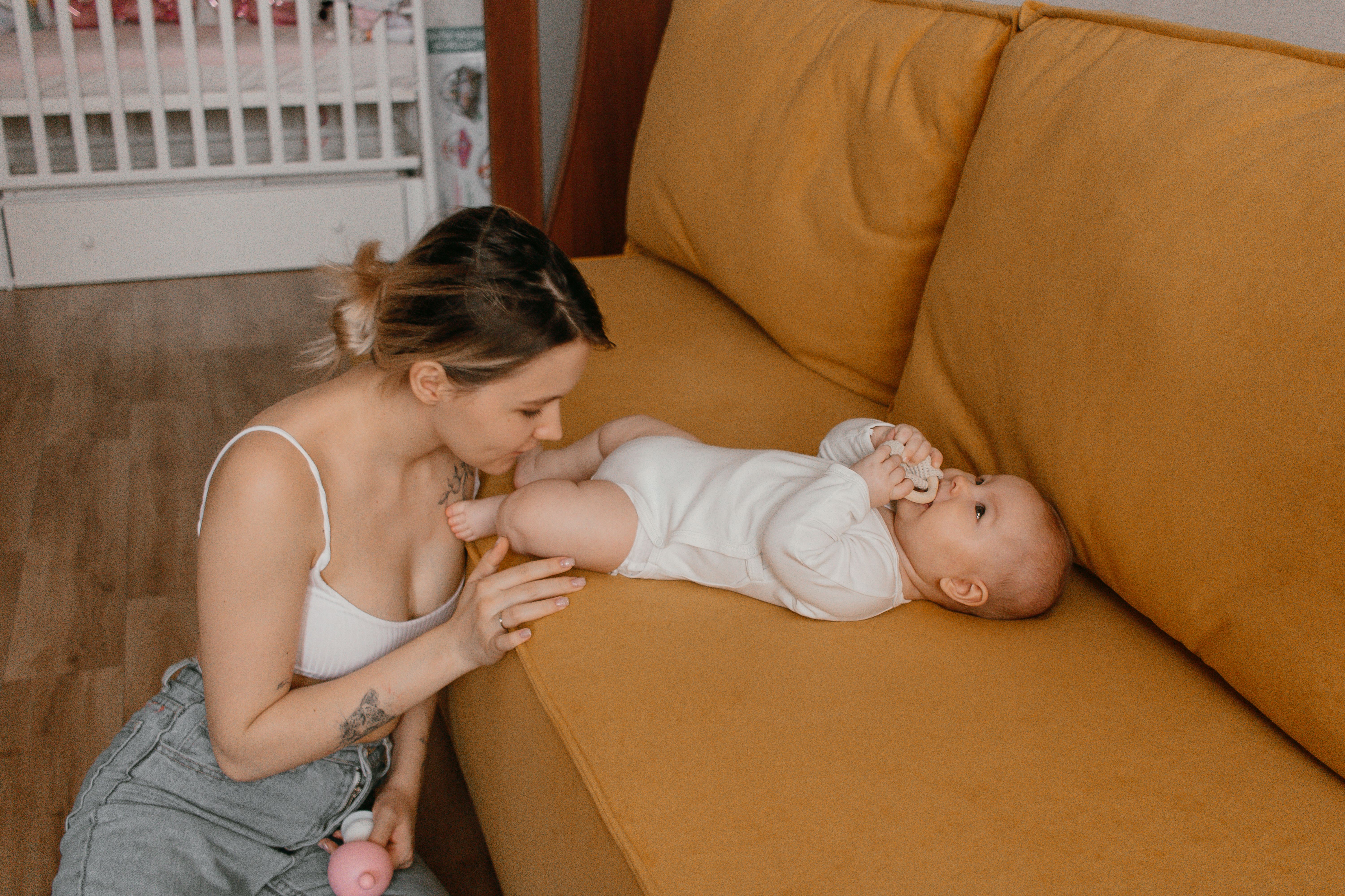A mother sitting beside her baby on a couch, enjoying a tender moment indoors.