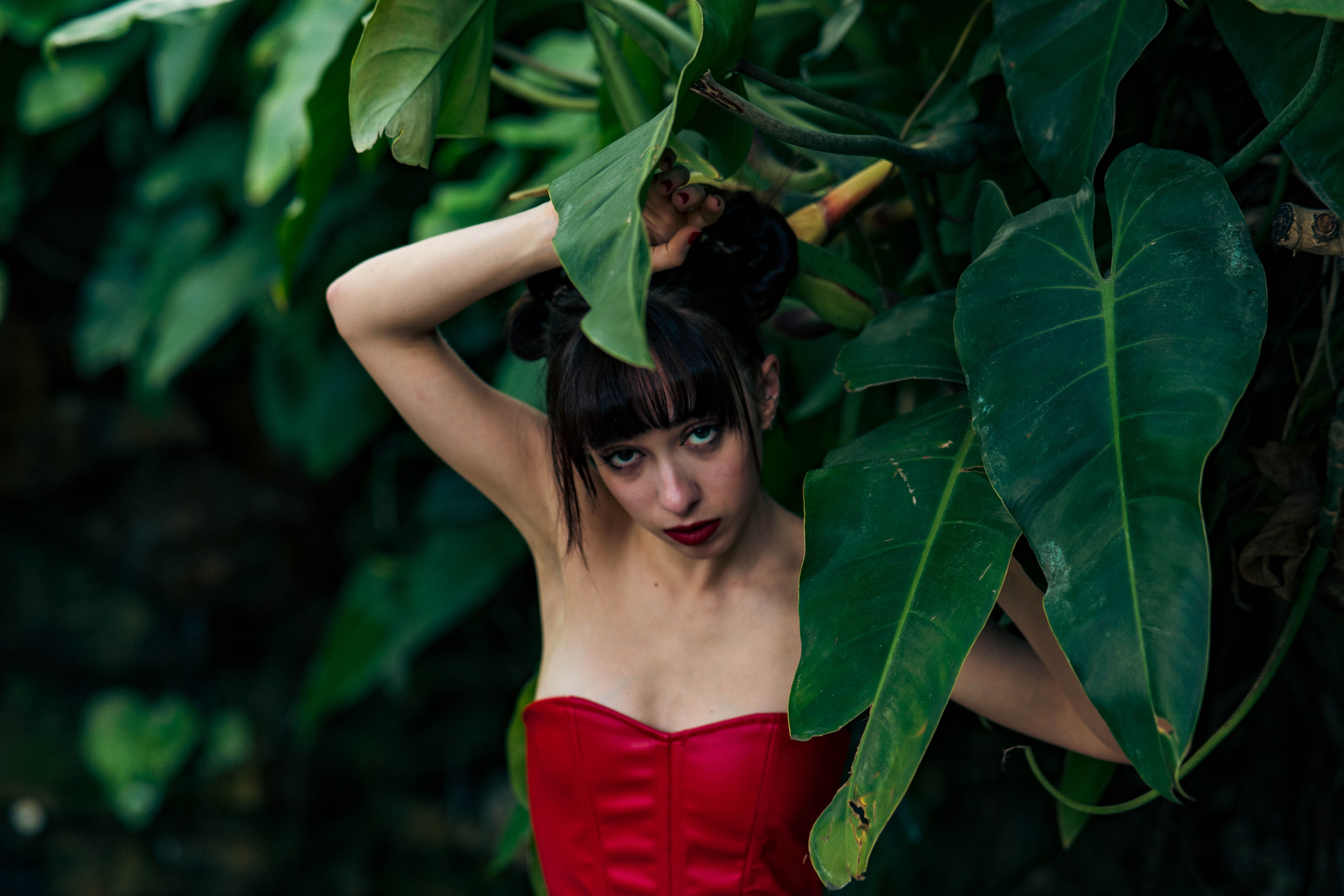 Striking fashion portrait in nature with vibrant red dress and lush green background.
