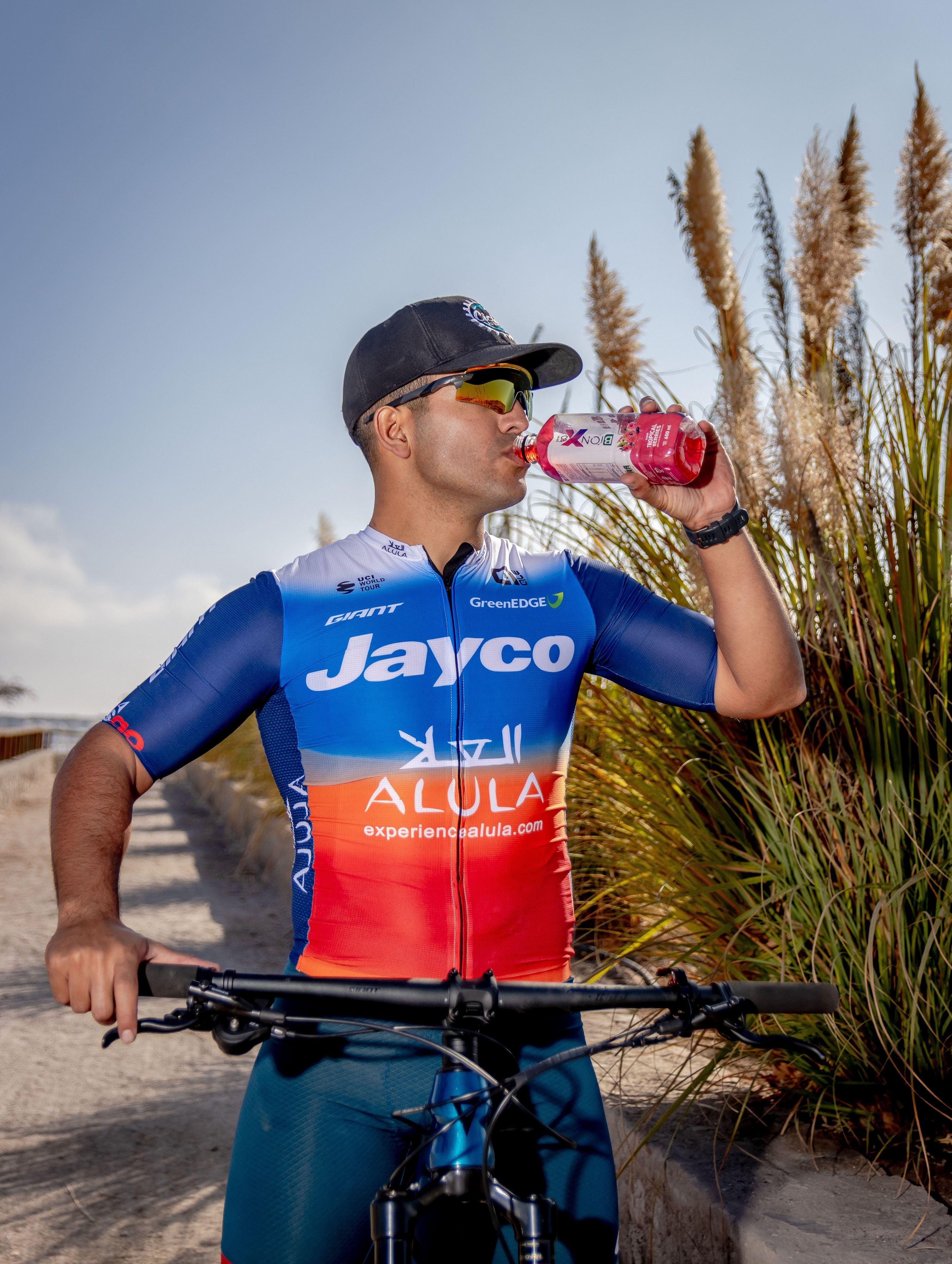 A sportsman in team gear drinks from a bottle while cycling outdoors in Alto Hospicio, Chile.