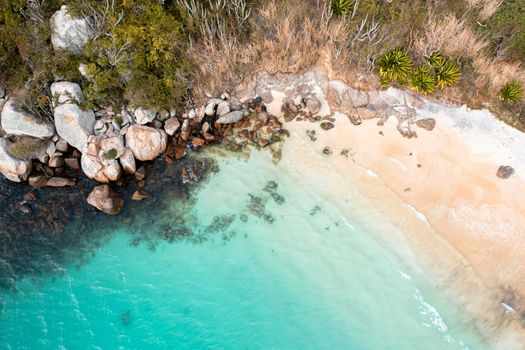 Top view of a serene beach with clear turquoise waters, rocks, and vegetation.