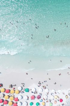 Aerial view of a sunny beach with colorful umbrellas and people enjoying the sea.