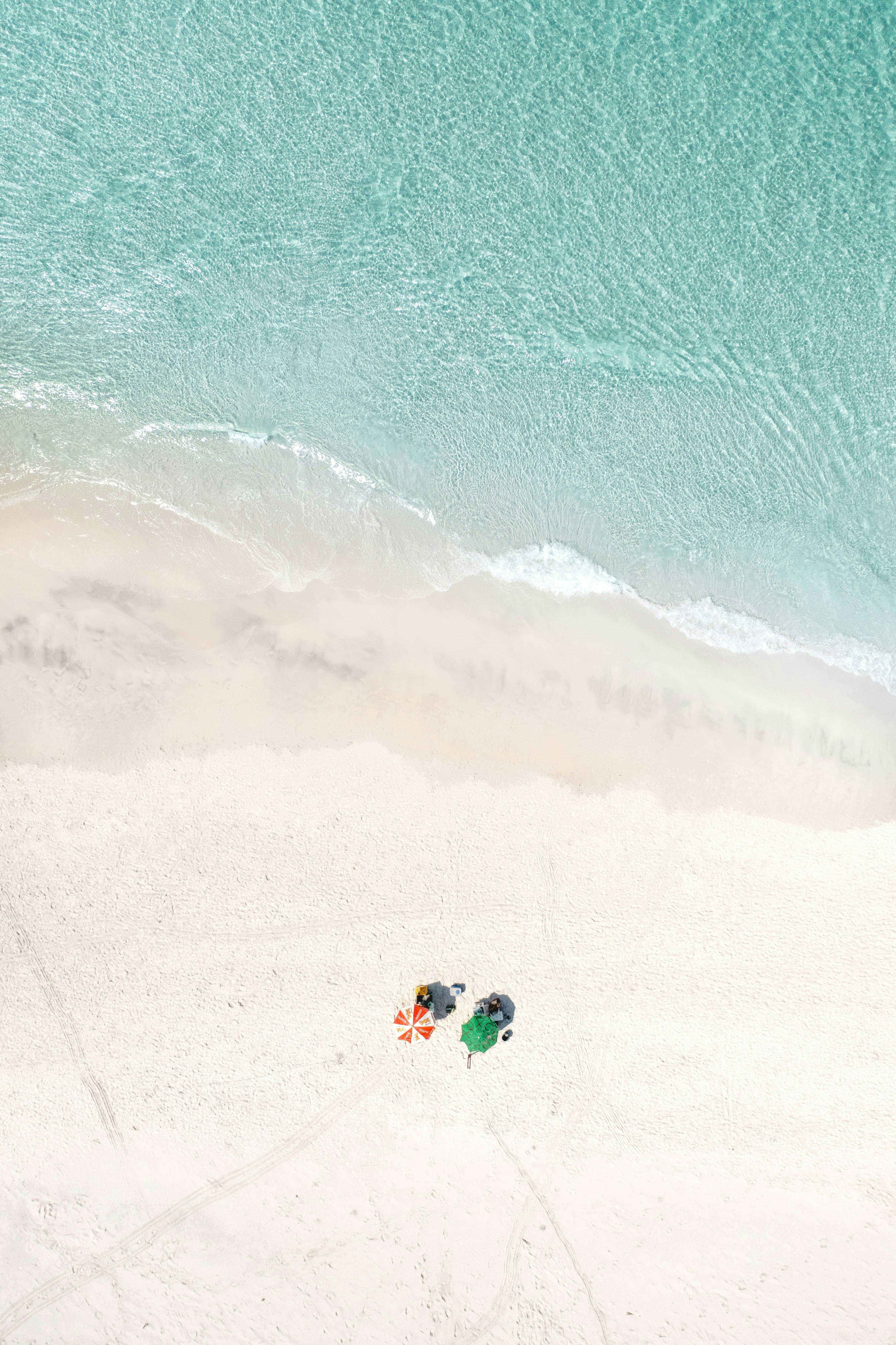 Aerial view of a pristine beach with vibrant umbrellas and tranquil ocean waves.