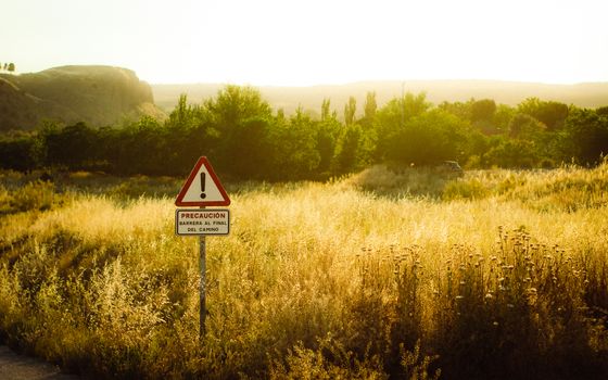 Golden sunset over a grassy field with a warning sign in Madrid, Spain.