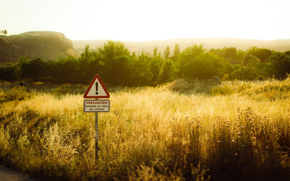 Atardecer dorado sobre un campo de hierba con una señal de advertencia en Madrid, España.