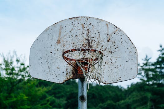 Close-up of a rusty outdoor basketball hoop with a weathered backboard set against a natural backdrop.