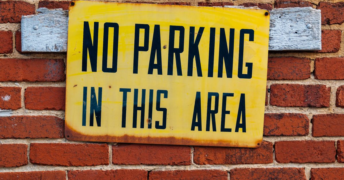 Bright yellow no parking sign attached to a red brick wall.